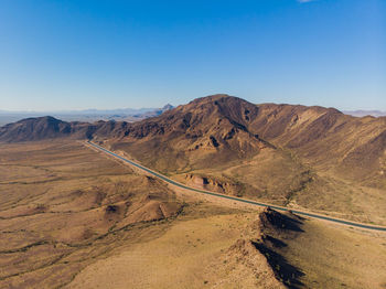 Scenic view of road by mountains against clear blue sky