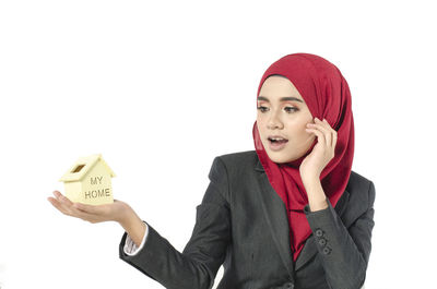 Surprised businesswoman holding house model against white background