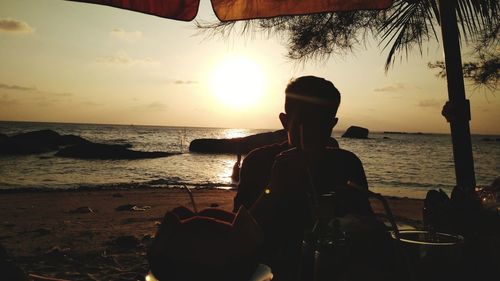 Rear view of men sitting at beach during sunset