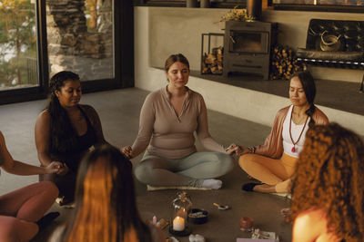 Multiracial female friends holding hands while doing meditation at retreat center