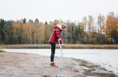 Injured woman stood at the beach with crutches looking thoughtful