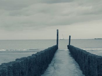 Wooden posts in sea against sky