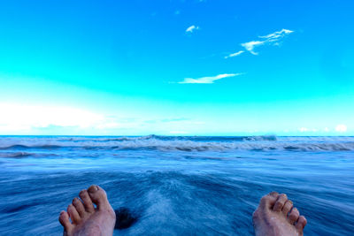 Low section of person in sea against blue sky