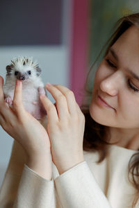 Girl holds cute hedgehog in her hands. portrait of pretty curious muzzle of animal. favorite pets. 