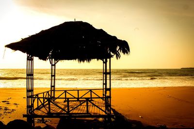 Silhouette built structure on beach against sky during sunset