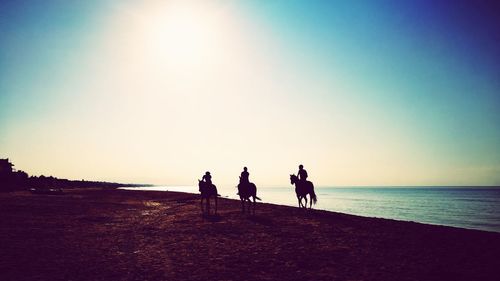 Silhouette people walking on beach against clear sky