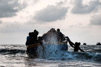 Waves splashing in sea against cloudy sky