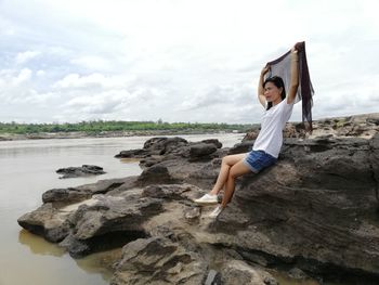 Young woman on rock at beach against sky