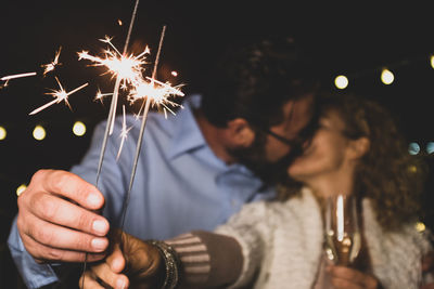 Couple kissing while holding sparklers at night