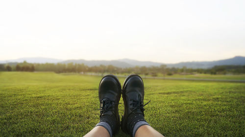 Low section of person relaxing on field against sky