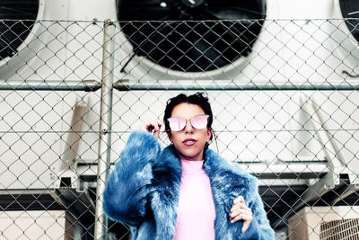 Portrait of woman wearing sunglasses against chainlink fence