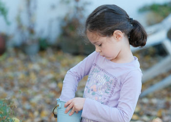 Young girl collecting fallen leaves into a small blue bucket while plaing in the backyard