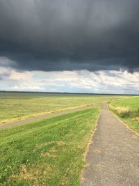 Road passing through field against cloudy sky