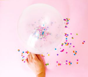 Close-up of hand holding balloons against white background