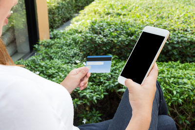 Cropped image of woman online shopping using phone in yard