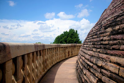 Empty footpath by wall against sky