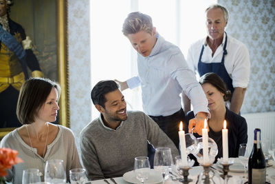 Waiter serving water to business people at restaurant with chef standing in background