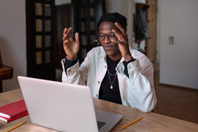 Smiling young african man tutor wearing wireless earbuds talking by webcam teaching online from home