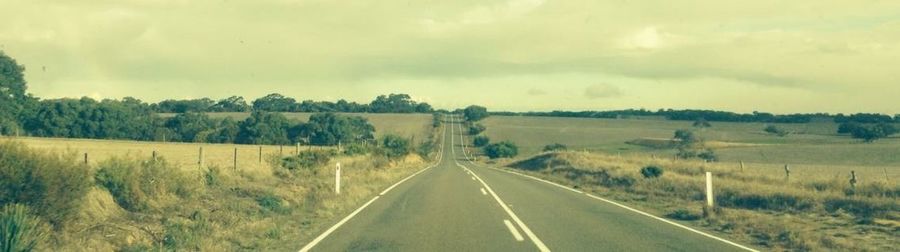 Road passing through field against cloudy sky