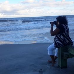 Full length of woman photographing through camera at beach during sunset