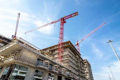 Low angle view of crane by building against sky