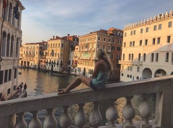 Woman sitting by railing in city against sky