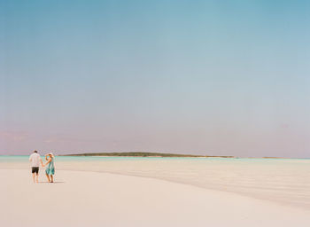 People walking on beach against clear sky