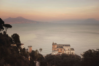 High angle view of buildings by sea against sky during sunset