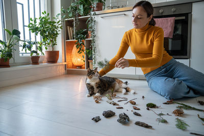 Caring woman sitting on floor with cat, giving twig to sniff to prevent domestic pet dementia