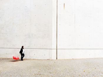 Full length of woman with red balloons walking against wall