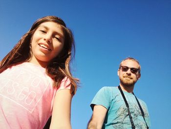 Low angle view of father and daughter standing against clear blue sky