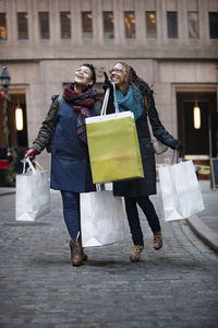 Happy women holding shopping bags while standing at street