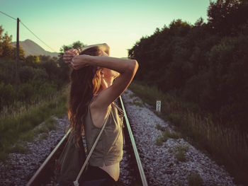 Side view of woman standing on railroad track against sky