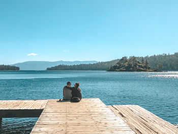 People sitting by lake against sky