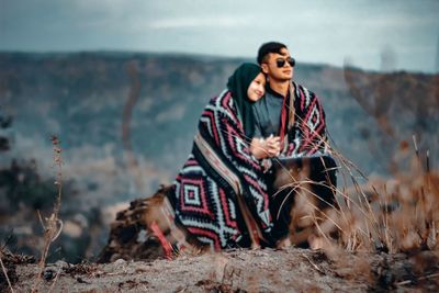 Young man sitting on land against sky