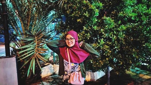 Portrait of young woman standing against trees