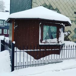 Snow covered house by fence against mountain