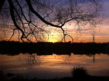 Silhouette bare tree by lake against sky during sunset