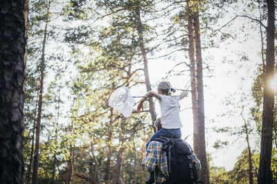 Rear view of father with backpack carrying daughter on shoulder in forest