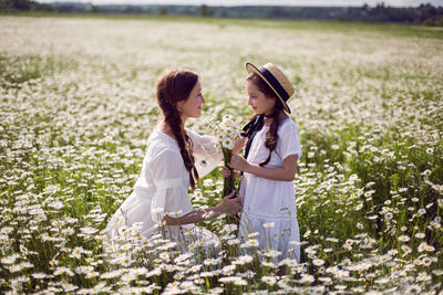 Mother with daughter in a white dress and hat stand in a daisy field in summer