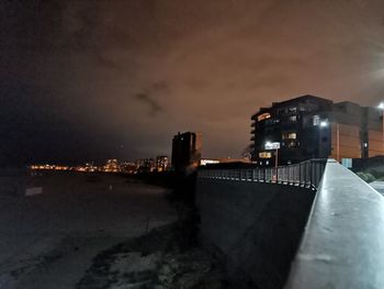 Illuminated buildings by river against sky at night