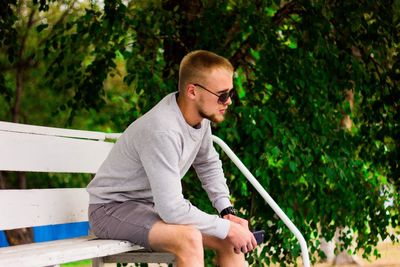 Side view of young man sitting on bench in park