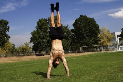 Shirtless man doing handstand on field against sky