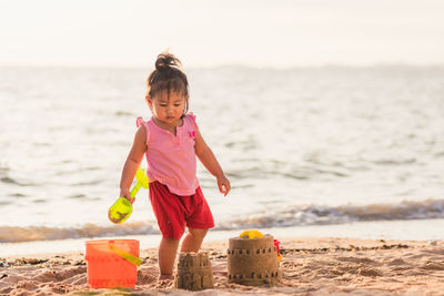 Full length of girl standing by sandcastle at beach