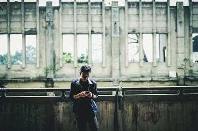 Young man using mobile phone against abandoned building