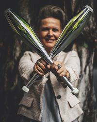 Portrait of smiling woman holding juggling clubs outdoors