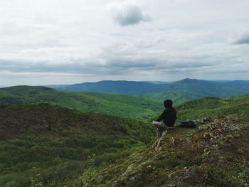 Rear view of man sitting on land against sky