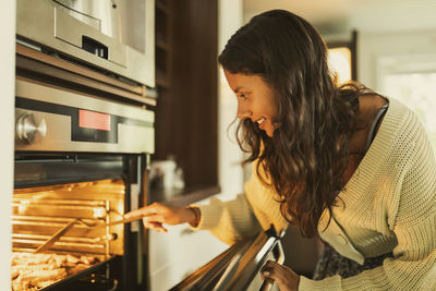 Smiling girl checking food while opening oven door