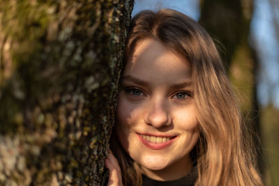 Portrait of young woman by tree trunk