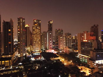 Illuminated modern buildings in city against sky at night